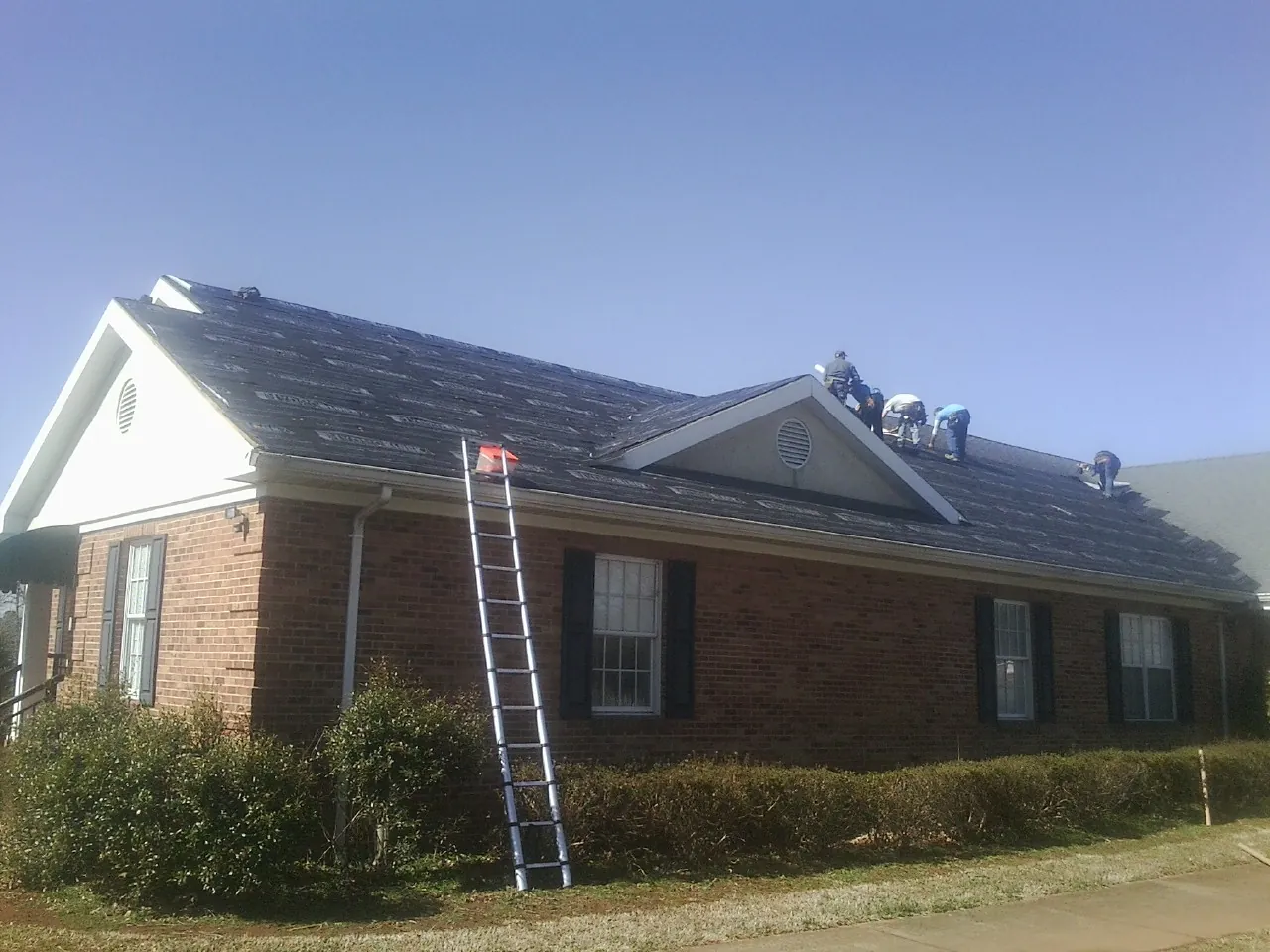 Crew tearing shingles off a brick ranch roof with a ladder set — Emergency Roof Repair work by our crew in Amelia