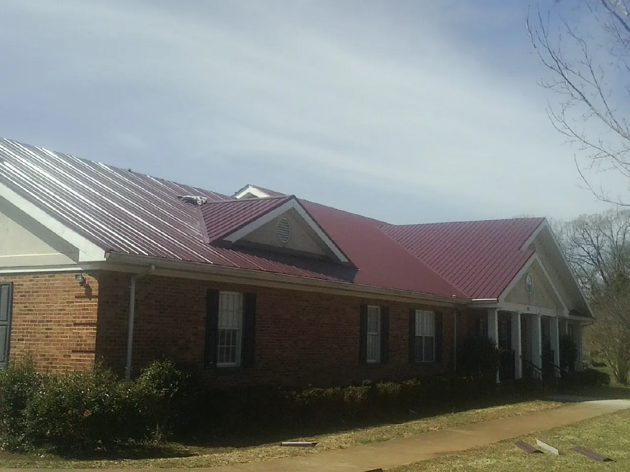 Red metal roof with gabled entries on a long brick building, from a Hail Damage Roof Repair job in Amelia