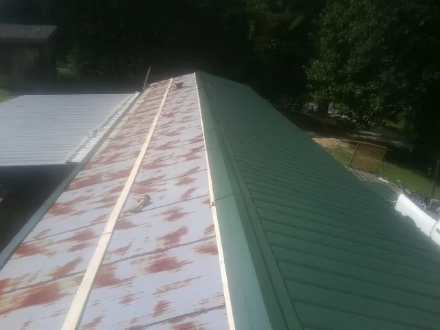 Old rusted panels beside newly installed green metal roofing — Wind Damage Roof Repair by Roofing Brothers in Amelia