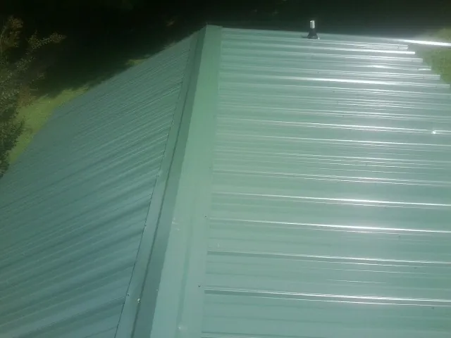 New green metal panels meeting at the ridge of a roof — Flat Roof Repair work by our crew in Amelia