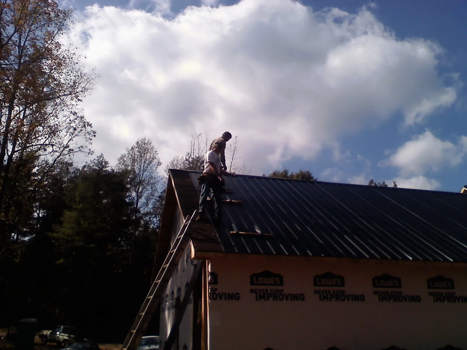 Roofer fastening dark metal panels high against a cloudy sky, from a Roof Inspection job in Amelia