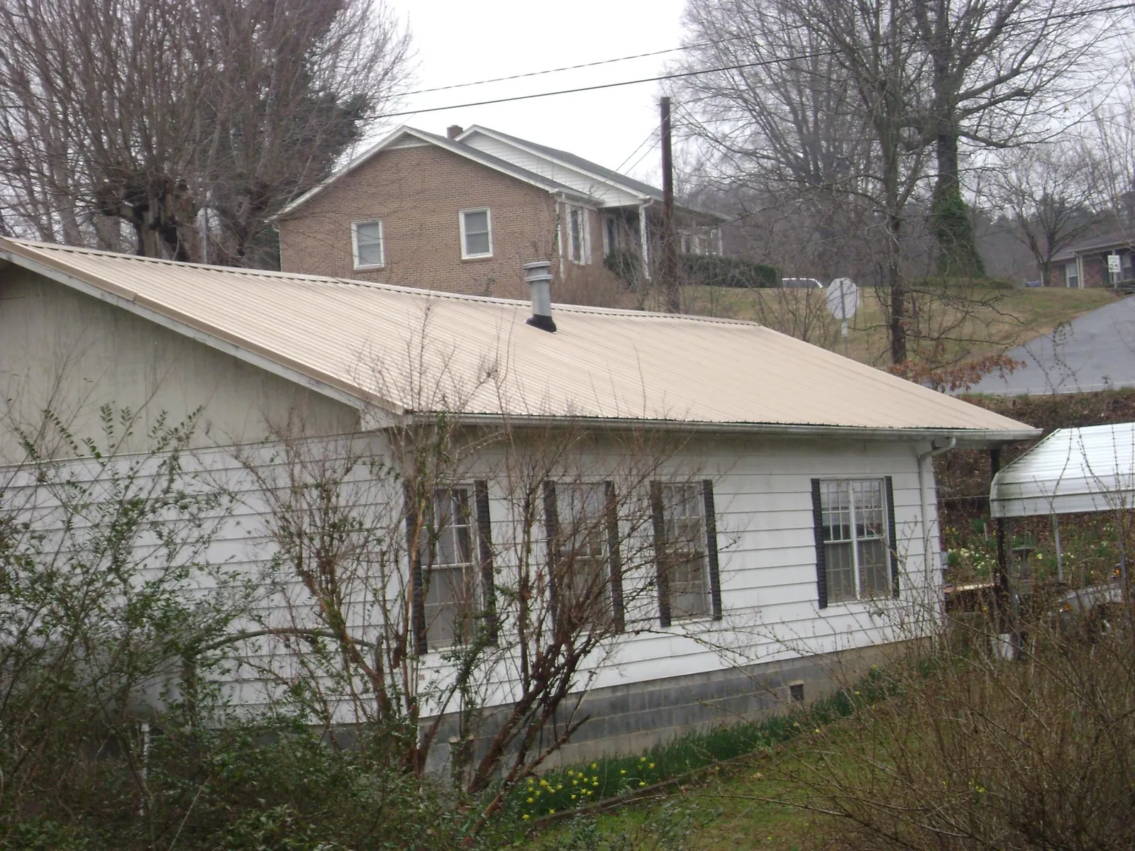 Tan metal roof on a white sided house set into a hillside — Commercial Roofing by Roofing Brothers in Amelia