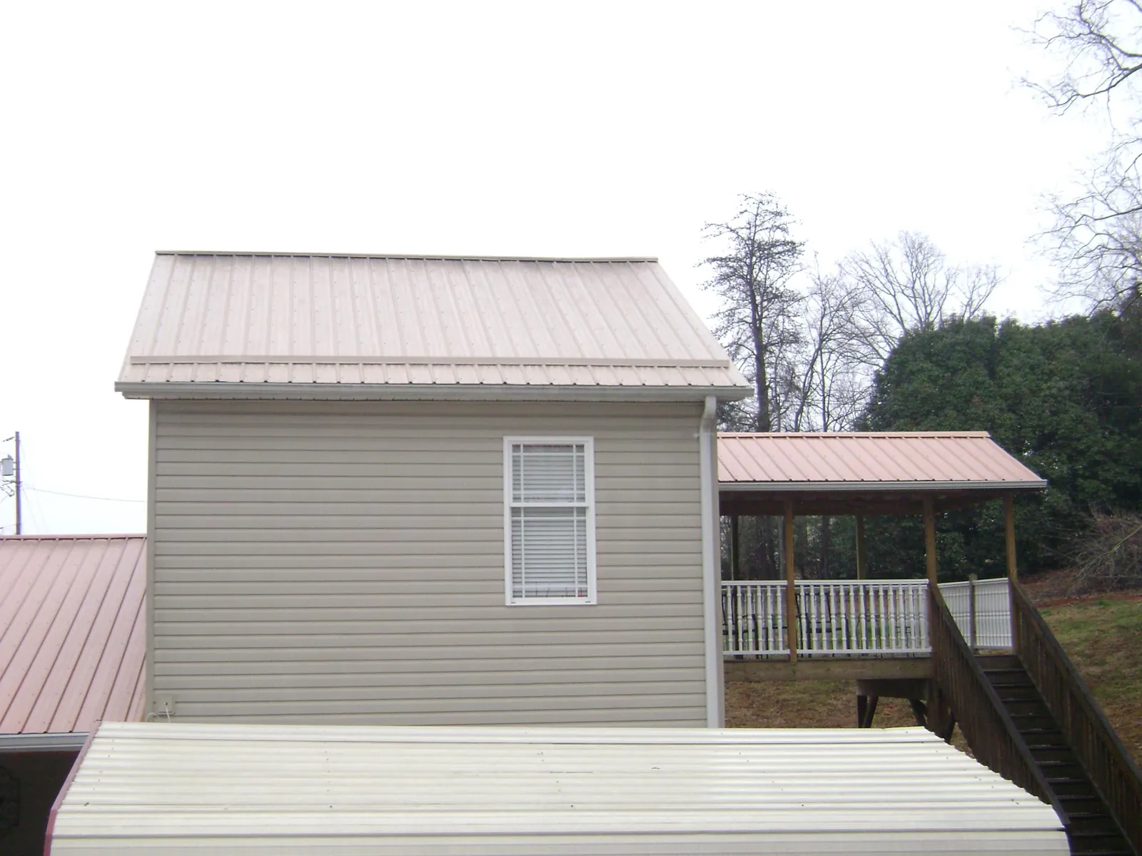 Tan metal roofs on a two story addition and attached porch, from a Roof Replacement job in Amelia